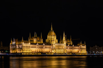 Fototapeta premium Stunning view of the Hungarian Parliament Building at the bank of River Danube at night in Budapest, Hungary