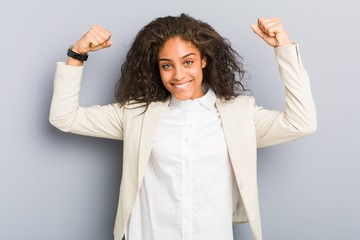 Young african american business woman showing strength gesture with arms, symbol of feminine power