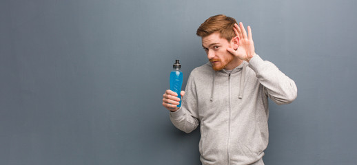 Young redhead fitness man try to listening a gossip. He is holding an energy drink.