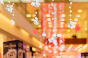 Blurred interior of shopping center or mall festively lit and decorated with shiny red white garlands. Background for holiday, Christmas and New Year. With bokeh
