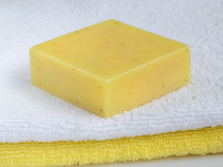 Yellow handmade lemon soap bar on a terry cotton towel. Natural toiletries and hygiene products with herbs and essential oils.