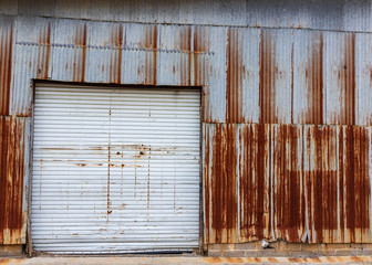 A photo of a building with a white garage door and rusted steel siding.
