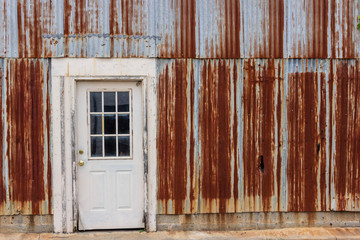 A view of the front of a building with a white door and rusted steel siding.