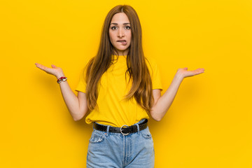 Young ginger redhead woman confused and doubtful shrugging shoulders to hold a copy space.