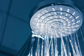 Obraz na płótnie Canvas Close up of a modern shower head with sprinkling water, blue toned photo.