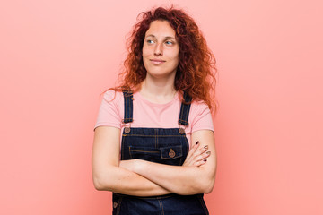 Young pretty ginger redhead woman wearing a jeans dungaree smiling confident with crossed arms.