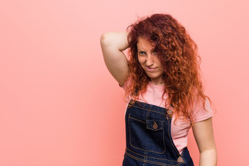 Young pretty ginger redhead woman wearing a jeans dungaree touching back of head, thinking and making a choice.