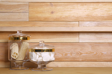 Composition of glass jar with cotton pads on table near wooden wall. Space for text
