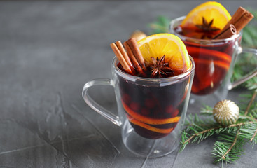 Glass cups with mulled wine and fir branches on grey table. Space for text