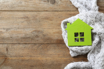 House model and scarf on wooden background, top view with space for text. Heating efficiency