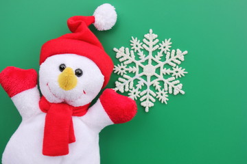 Toy smiling snowman and snowflake on a green background.