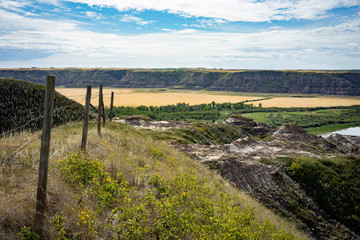 Hill with old fence facing large sedimentary rock canyon with pastures  © Anthony