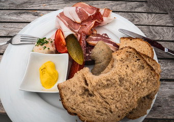 View from above of delicious Vesper German traditional food plate with multiple sausages, bread, mustard, tomatoes, pickled cucumbers and pork fat