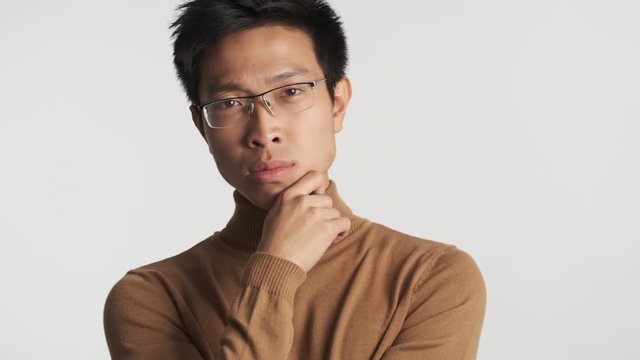 Young thoughtful stylish asian man in eyeglasses seriously looking in camera isolated. Thinking expression