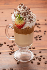Cold coffee drink frappe (frappuccino), with whipped cream and chocolate nibs, with grains of coffee on wooden background