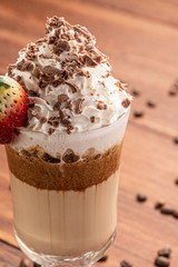 Cold coffee drink frappe (frappuccino), with whipped cream and chocolate nibs, with grains of coffee on wooden background