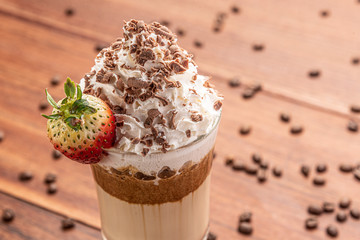 Cold coffee drink frappe (frappuccino), with whipped cream and chocolate nibs, with grains of coffee on wooden background