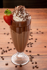 Cold coffee drink frappe (frappuccino), with whipped cream and chocolate nibs, with grains of coffee on wooden background