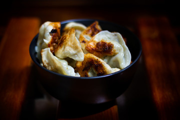 Pan fried chicken and prawn dumplings in a black bowl on a brown wooden table