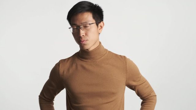 Young serious asian guy in eyeglasses confidently waving head. Sure no gesture over white background