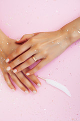 beautiful manicured woman hands with white feather on pink background, wearing wedding ring