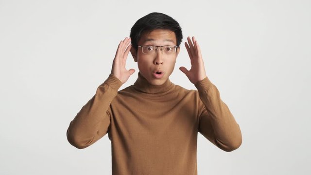 Young afraid asian man in eyeglasses scaredly looking in camera isolated. Wow expression