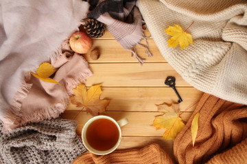 cup of hot fragrant tea, autumn leaves, apple, cozy scarves and knitted sweaters, key, flat, concept of hugg, winter or autumn mood