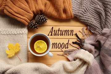 cup of hot fragrant tea with lemon, autumn leaves, apple, cozy scarves and knitted sweaters, flat, concept hugge, autumn mood