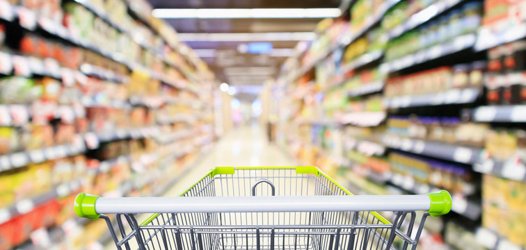 Empty green shopping cart with supermarket aisle interior with product shelves abstract blur background