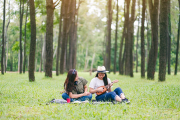 Two women playing ukulele while sitting together in the woods