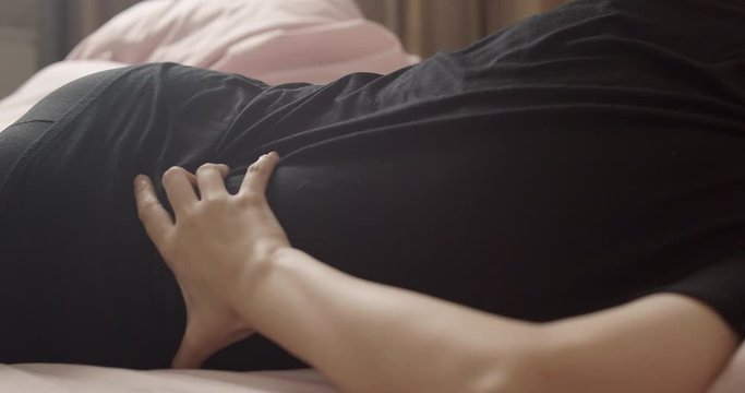 Asian woman having pelvic pain stomachache Medical and health care concept. hands holding on stomach as suffering from menstruation while sitting on bed at home.  
