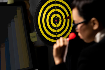 Tomboy Manager CEO looks at Dartboard and hold dart to throw as it is Growth of Business to achieve Objective Target goal for next year.  She works hard till late night