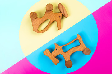 Multi-colored flat lay with eco-friendly wooden toys rabbit with carrot, dog with a bone on pink, blue and yellow isolated background.  Top view, template for kids learning and entertainment