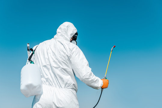 exterminator in white protective uniform holding toxic spray outside