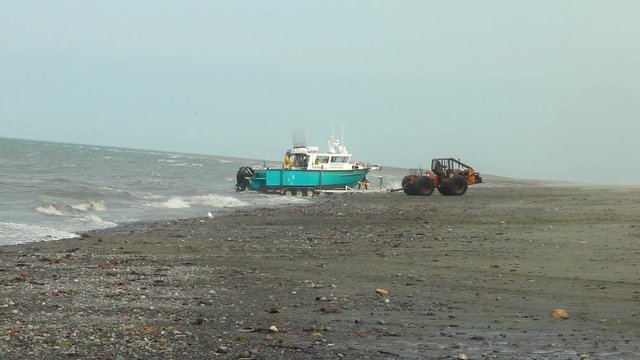 Tractor on  the beach towing a fishing charter boat out of  ocean at Anchor Point, Alaska.