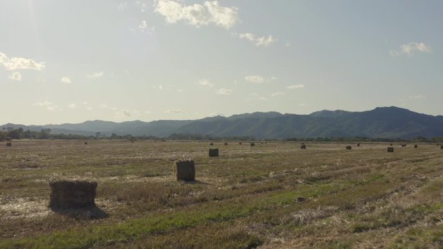 Fly over haystacks in the countryside field with mountain ridge in the background on a bright, clear, sunny day. Russia, Far East