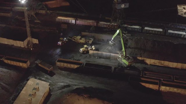Midnight coal cargo loading operations at coal terminal port, with cargo railway carriages, moored general cargo ships, port machinery and cranes in operation. Aerial shot. Russia, Far East.