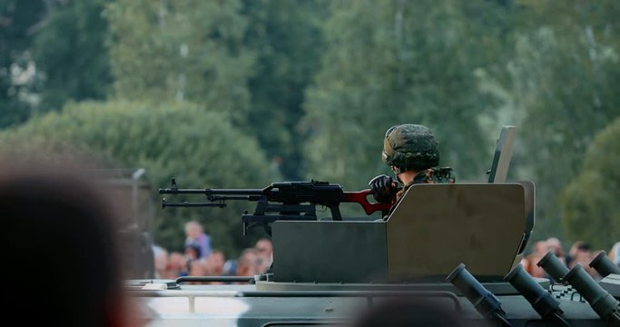 Military man in uniform sitting on an armored car. War vehicle in camouflage with a machine gun on the roof. Independence Day military parade in the CIS country. Urban life. Belarus 3 July 2019.