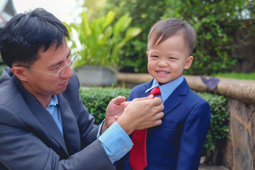 Asian father and son dressed in suits, Businessman helping his little child tying the necktie,...