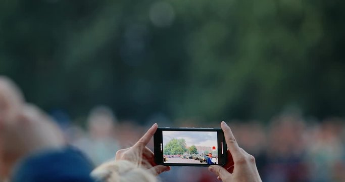 Woman hand with smartphone shoots war parade. Military vehicle in camouflage with a machine gun on the roof. Independence Day military parade in the CIS country. Urban life. Belarus 3 July 2019.