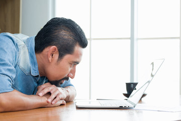Asian bearded Business Owner staring at the laptop screen while bend down and chin putting on back...