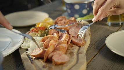 CLOSE UP: Friends sit at the picnic table and eat sausage on the cutting board