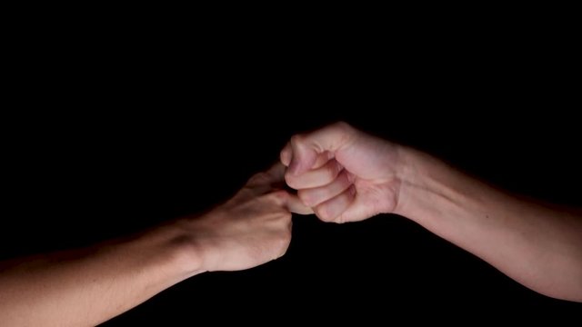 Slow motion shot of two hands playing each other in Rock Paper Scissors. Rock beats Scissors. The hands are illuminated in front of a black background. 