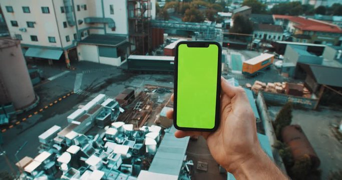 Man staying at factory backyard using smartphone checking internet news outdoor. Close-up.