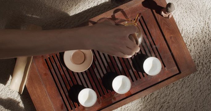 Top view video shot of beautiful Chinese tea ceremony inside sunny apartment slow motion. Male hands pouring fresh steaming drink into glass kettle close up. Traditional ware equipment atmosphere