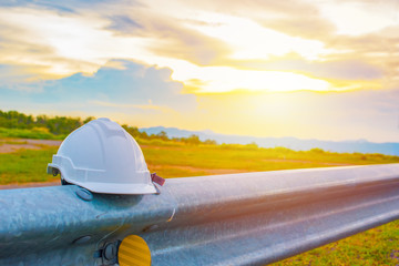 Close up of white safety helmet placed on roadside steel, Steel guard rail barrier with sunset background, Helmet in construction site after work during the sunset, Safety and Engineering concept.