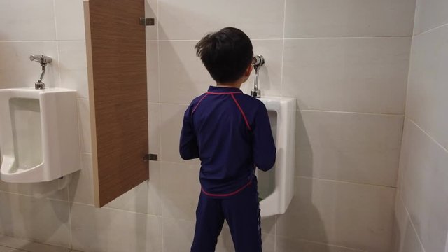 the boy peeing to toilet bowl in restroom