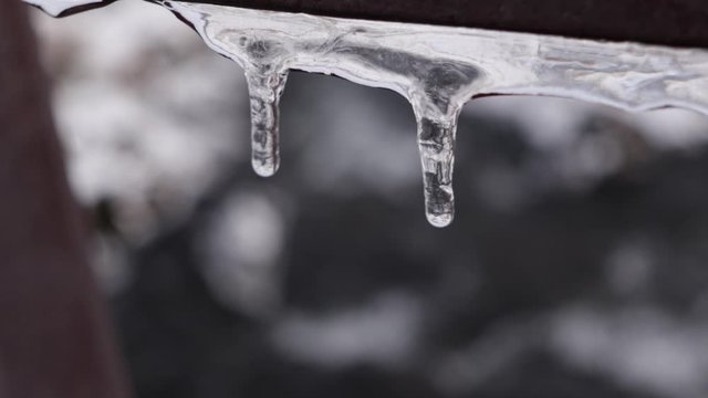Water slowly dropping from an icy stalactite hanging on a fence with a river in the background. Iceland in winter.