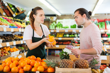 Young woman selling fresh oranges to man