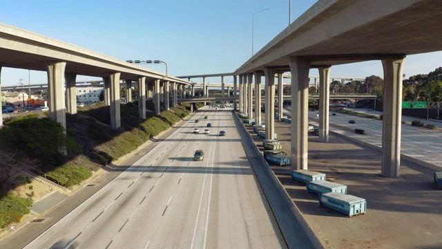 Front view to the groung level of the expressway. Drone moves under the road brige between the road supports from one line to the opposite. Cars move to and from the camera.